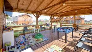 Un espacio al aire libre techado con suelo de madera, asientos y una mesa de fútbol de mesa.