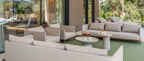 A modern living room with a sofa set, a coffee table, and a glass door leading to a balcony with outdoor furniture.