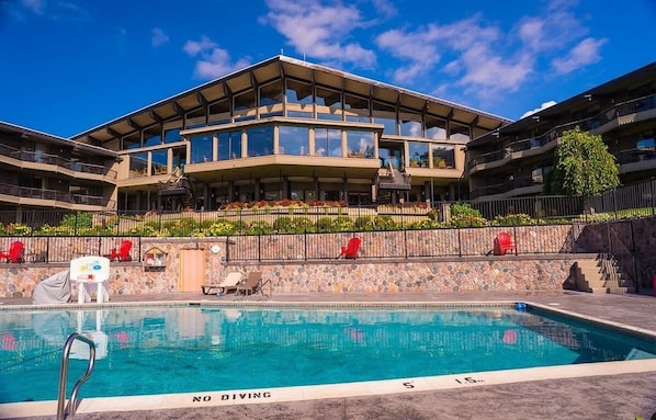 A modern hotel with a pool, outdoor seating, and a stone facade.
