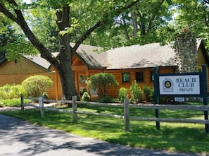 A wooden cabin with a stone chimney, surrounded by lush greenery and a wooden fence. - Shanty Creek, Private Beach Club (Bellaire)