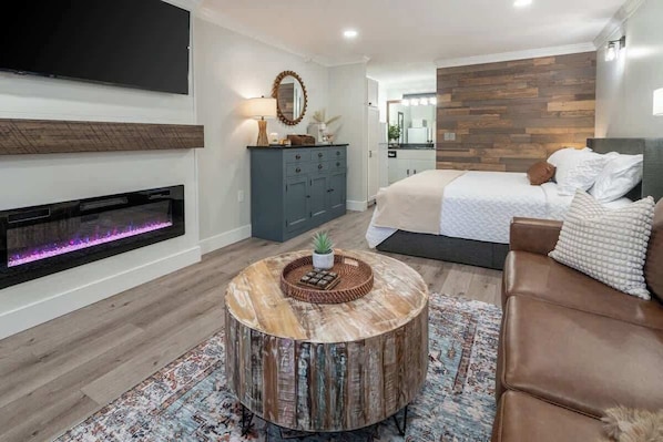 A modern living room with a fireplace, a round coffee table, a sofa, and a bed with a headboard.
