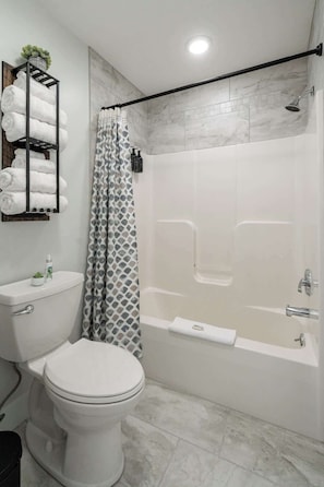 A modern bathroom with a toilet, a shower with a glass door, and a towel rack with folded towels.