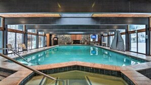 Une piscine intérieure dotée d’un plafond en bois, de murs en pierre et de grandes fenêtres.