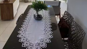 A modern dining area with a long table, white lace table runner, and a potted plant. - Beach House in Barra, Ilhéus (Barra do Itaípe Ilhéus)