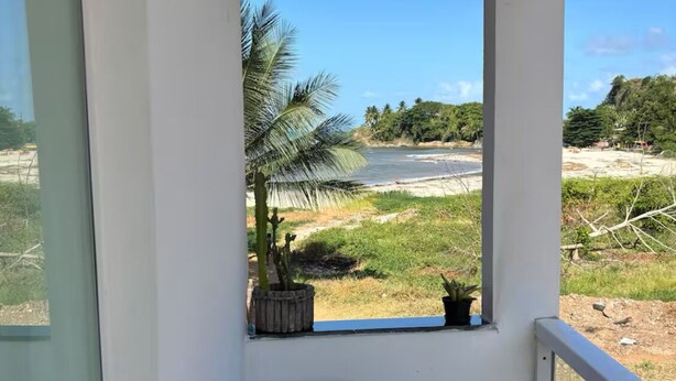A balcony with a glass table and chairs, overlooking a beach with palm trees and a clear sky. - Beach House in Barra, Ilhéus (Barra do Itaípe Ilhéus)