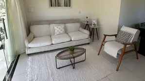 A living room with a white sofa, a round coffee table, a wooden chair, and a hanging light fixture. - Beach House in Barra, Ilhéus (Barra do Itaípe Ilhéus)