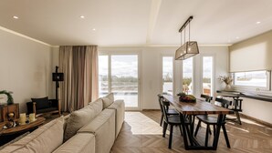 Una sala de estar moderna con un sofá grande, una mesa de comedor y sillas. Una ventana grande ofrece vistas al exterior.