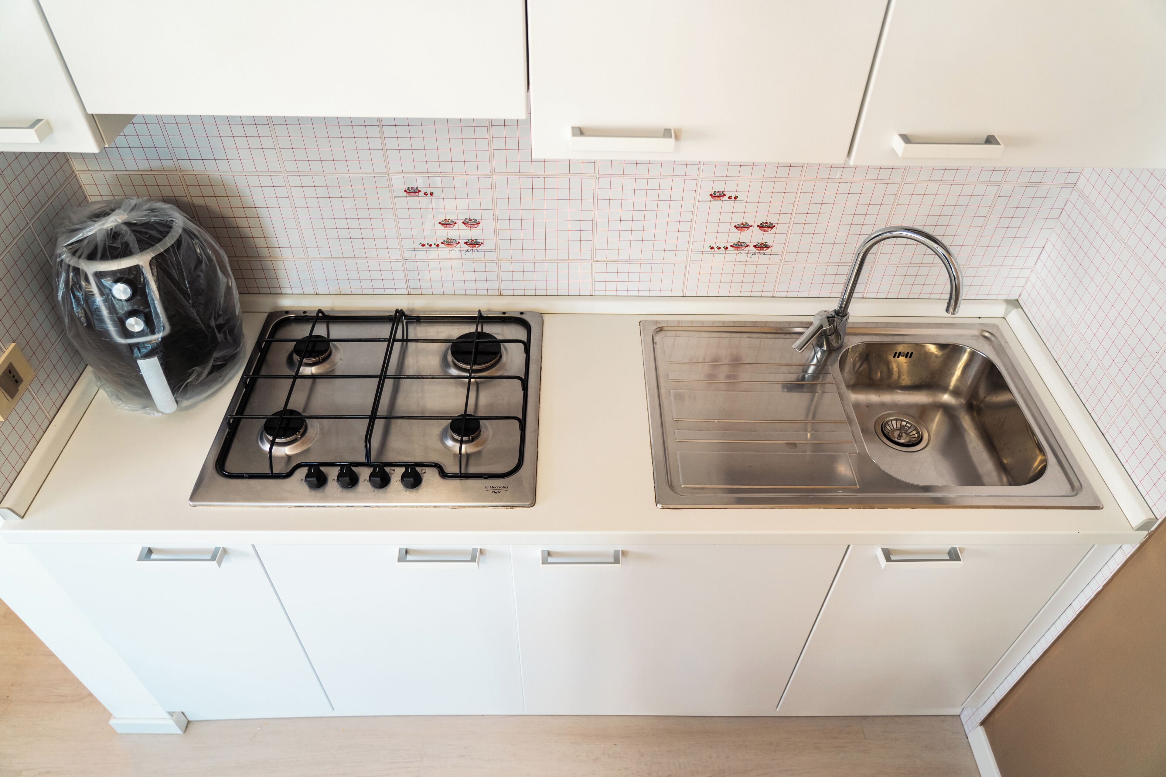 A kitchen with a gas stove, stainless steel sink, and white cabinets.
