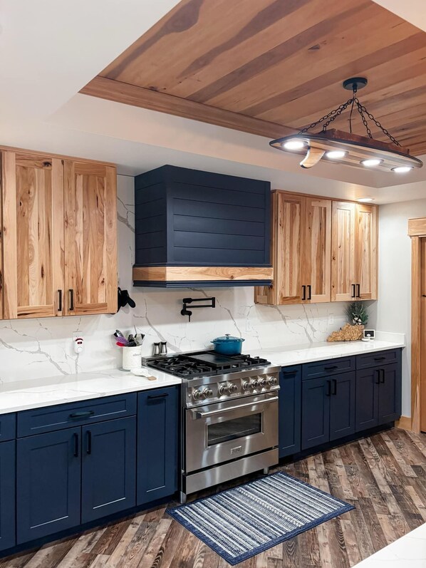 A modern kitchen with wooden cabinets, a stainless steel stove, and a marble countertop.