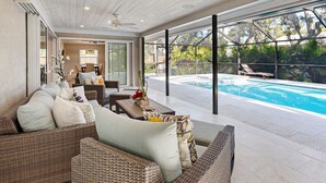 A spacious patio with a pool, wicker furniture, and a ceiling fan.