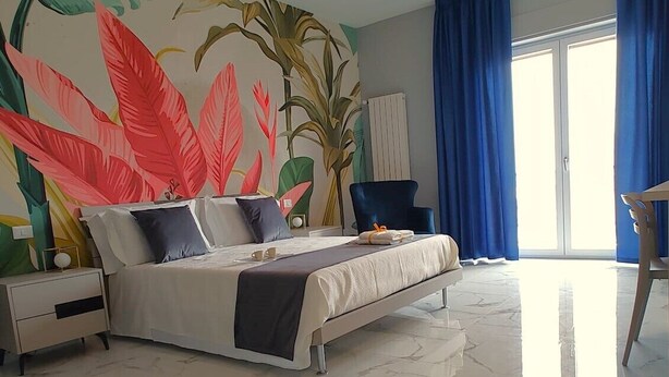 Een moderne slaapkamer met een groot bed, een nachtkastje, een stoel en een groot raam met gordijnen.