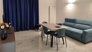 Een moderne woonkamer met een eettafel, een blauwe bank en een vaas met bloemen.