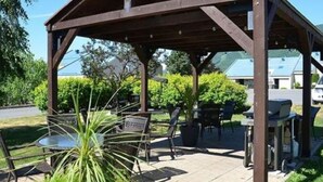 A covered outdoor seating area with tables and chairs, surrounded by greenery. - L'Agachoun - Ski & Bike 2mns from Mont St-Anne! (Saint-Ferréol-les-Neiges)