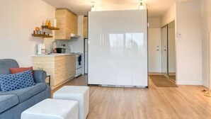 A modern apartment with a grey sofa, a white ottoman, a kitchen with white cabinets, and a large white wardrobe. - L'Agachoun - Ski & Bike 2mns from Mont St-Anne! (Saint-Ferréol-les-Neiges)