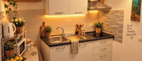 A modern kitchen with white cabinets, a stainless steel sink, and a black countertop. There are potted plants on the counter and a wall-mounted light fixture.