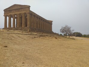 Un vaste temple antique, doté d’une façade imposante et de colonnes, situé sur une colline où la végétation est clairsemée.