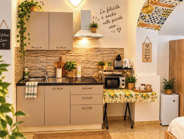 Een moderne keuken met een ingebouwde magnetron, waterkoker en een kleine koelkast. Er is een gootsteen met kraan, en diverse keukengerei en planten zijn zichtbaar.
