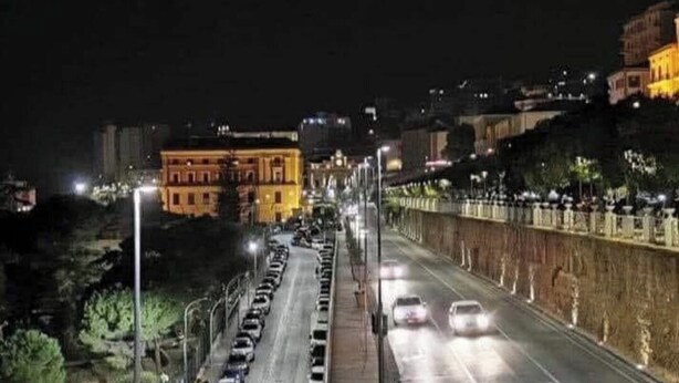 Une rue de la ville de nuit, avec des voitures garées, des lampadaires et des immeubles.