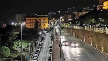 Rua urbana noturna com carros estacionados, postes de luz e edifícios.