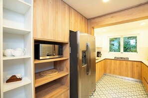 A compact kitchen with a built-in microwave, a stainless steel refrigerator, wooden cabinets, and a patterned floor.