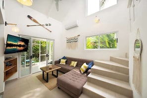 Un salon moderne avec un canapé marron, un téléviseur à écran plat, un escalier et une grande fenêtre donnant sur un paysage verdoyant.
