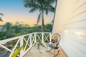 A balcony with a white railing, a black chair, and a palm tree in the background.