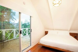 A bedroom with a bed, a sliding glass door, and a view of greenery outside.