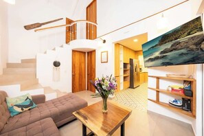 A modern living room with a sofa, a wooden coffee table, a staircase, and a kitchen area visible in the background. - Ocean Gardens: Private Retreat, Private Pool & BBQ (Esterillos Oeste)