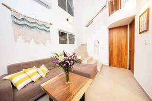 A modern interior with a sofa, a wooden table with a vase of flowers, a staircase, and a wooden door.