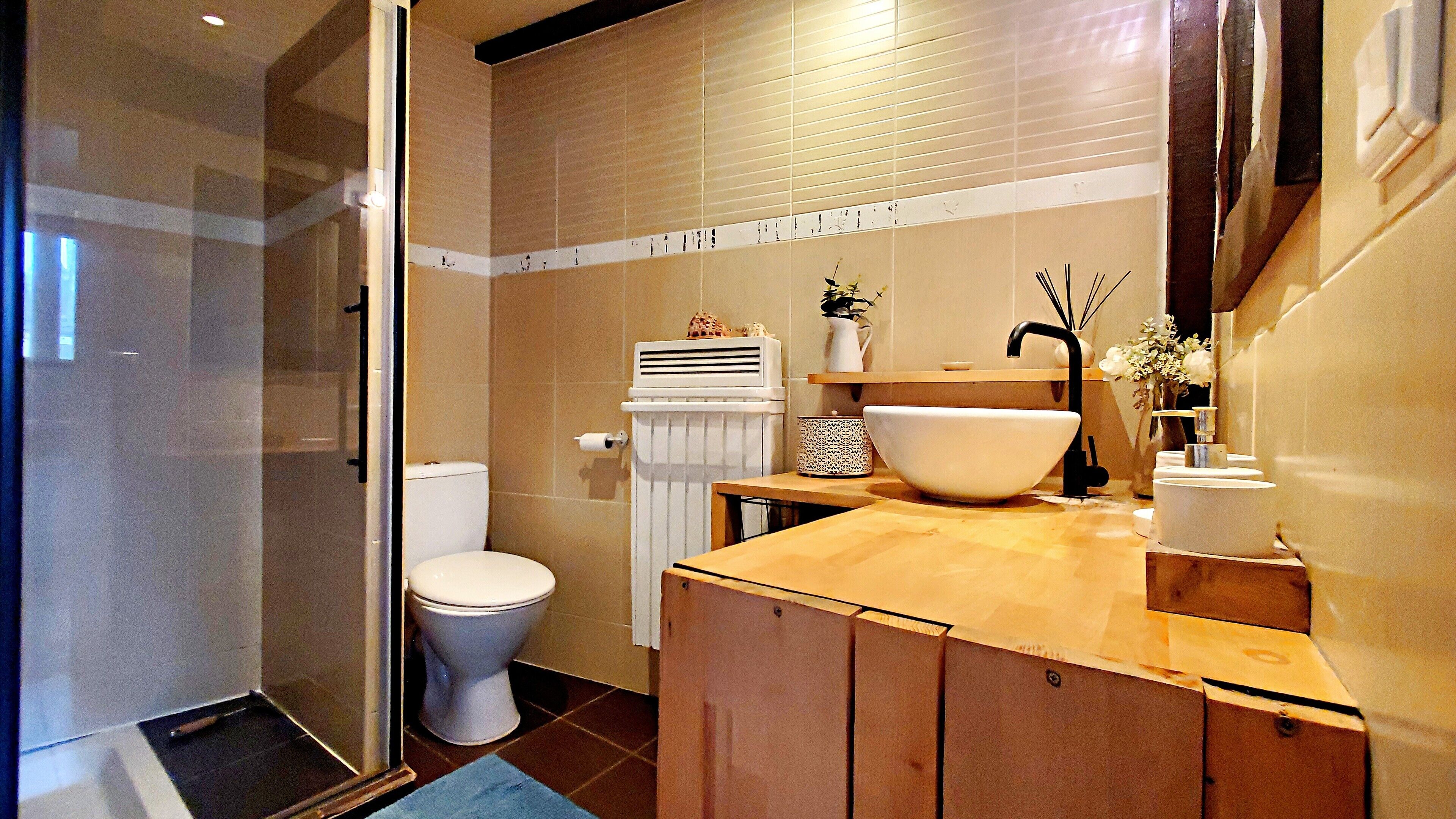 A modern bathroom with a glass shower enclosure, a toilet, a sink with a large basin, and a towel rack.