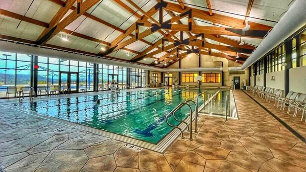 Une piscine intérieure dotée d’un sol carrelé en forme d’hexagone, de poutres en bois au plafond et offrant une vue sur l’extérieur grâce à de grandes fenêtres.