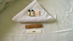 Un juego de artículos de aseo personal ordenado sobre una cama, con una almohada y una toalla blancos.