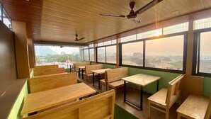Un aula con bancos y mesas de madera, amplias ventanas con vista a la ciudad y ventiladores de techo.