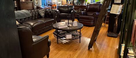A cozy living room with leather sofas, a coffee table, and a bookshelf filled with books.