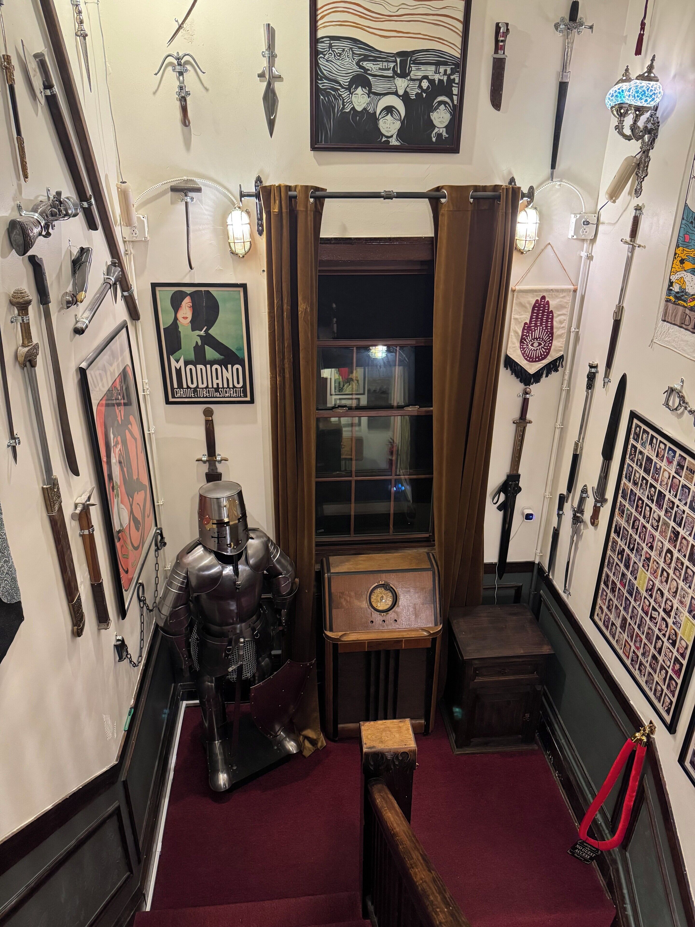 A room with a vintage decor, featuring a knight's armor, various weapons, and a small table with a clock.