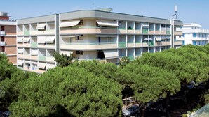 Un edificio de varios pisos con balcones, rodeado de árboles verdes y frondosos.