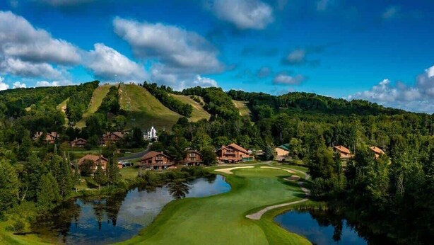 Un parcours de golf avec un étang, entouré de maisons et d’une colline sur laquelle se trouve un bâtiment.