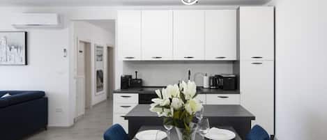 Een moderne keuken met witte kasten, een eettafel gedekt voor vier personen en een bloemenvaas.