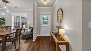 A dining area with a wooden table and chairs, a gray sofa, and a bench with a lamp. - Jacuzzi Tub-Walk to Dining & Shopping-Garage Parking (Tulsa)