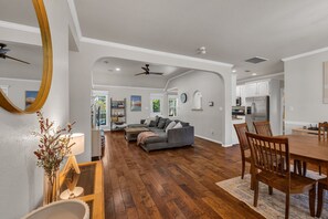 A spacious living room with hardwood flooring, a gray sectional sofa, and a dining area with wooden chairs and a table. - Jacuzzi Tub-Walk to Dining & Shopping-Garage Parking (Tulsa)