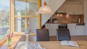 Una cocina moderna con una mesa de comedor, sillas, una lámpara colgante y una ventana con vistas a zonas verdes.