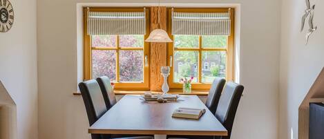 Un comedor con una mesa de madera, cuatro sillas, una lámpara colgante y una ventana con cortinas.