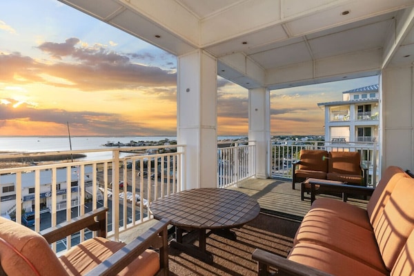 Spacious balcony lounge offers sunset views over the inlet and town, with comfortable seating, coastal breezes, and warm evening light, perfect for relaxing, dining, and enjoying the scenery.