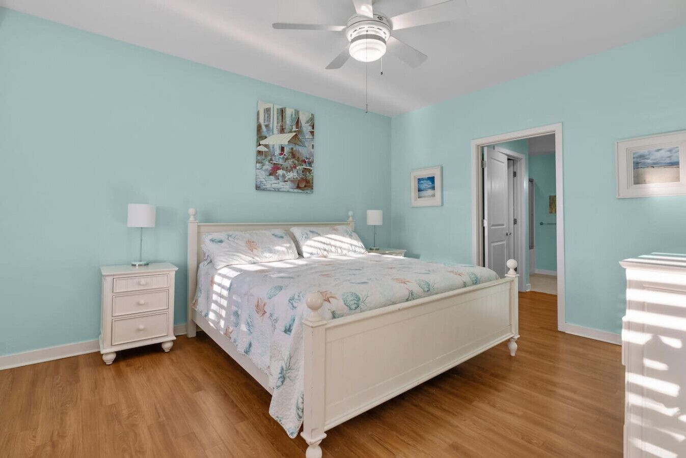 A bedroom with a bed, nightstands, a ceiling fan, and artwork on the walls.