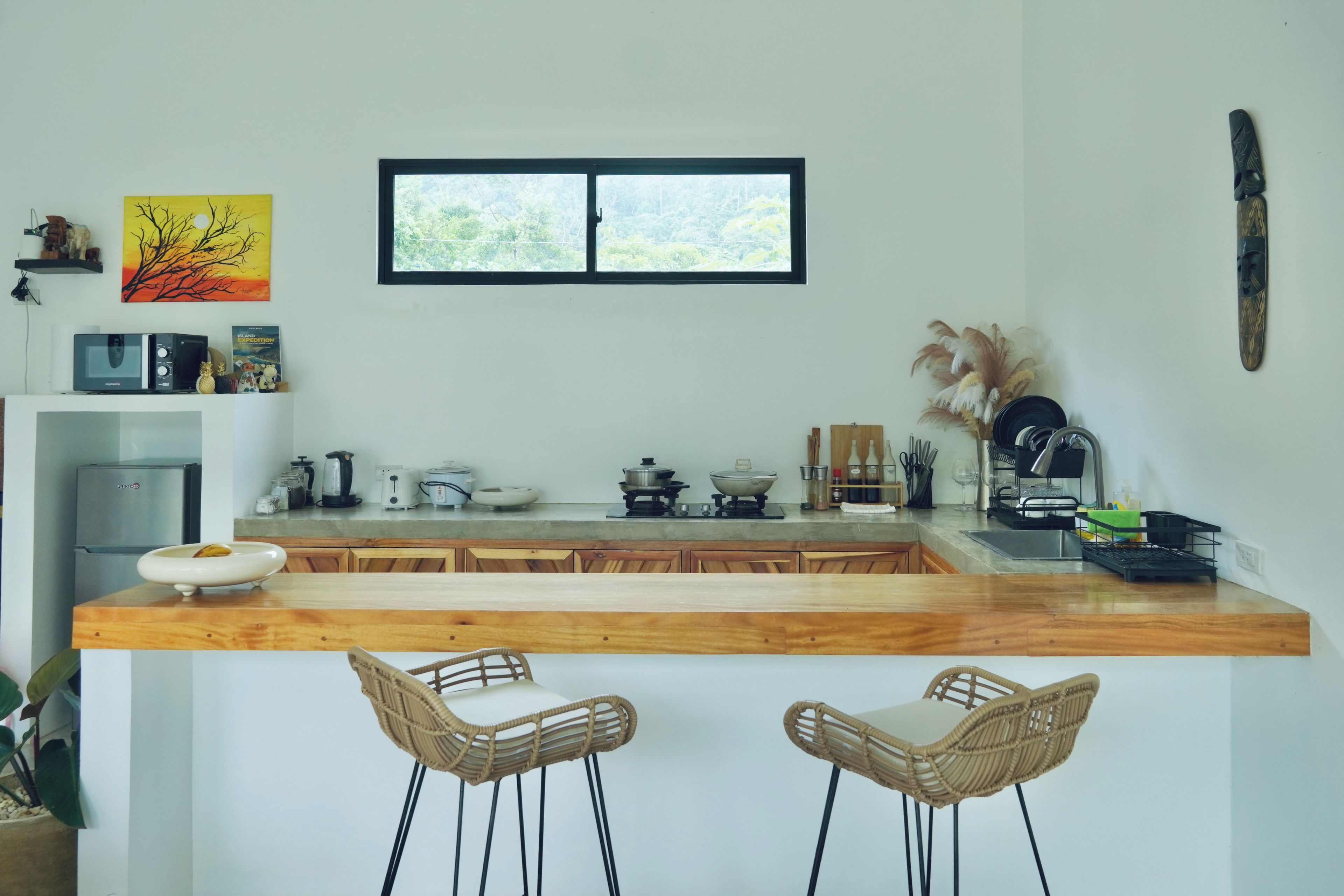 A kitchen with a wooden countertop, two wicker bar stools, a window above the sink, and various kitchen appliances.