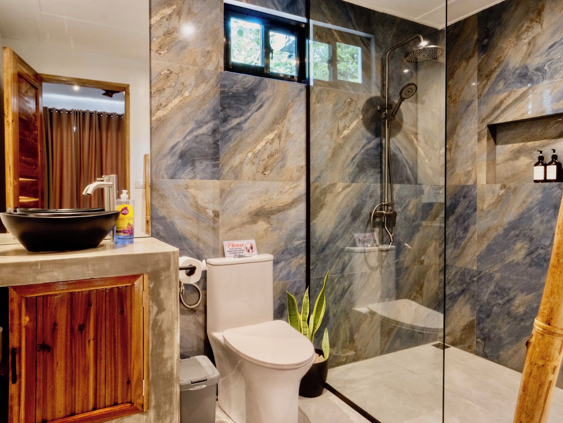 A modern bathroom with a marble wall, a glass shower enclosure, a wooden vanity, and a toilet.