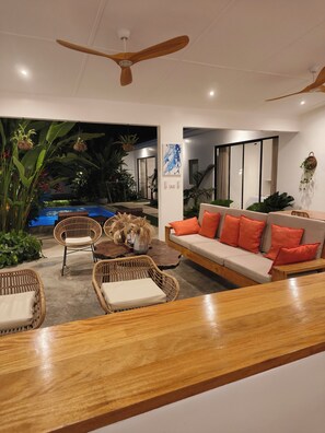 Una sala de estar moderna con piscina, muebles de mimbre y ventilador de techo.