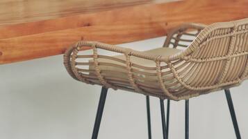 Una silla de mimbre con asiento y respaldo trenzados, sostenida por patas de metal negro, ubicada junto a una mesa de madera.