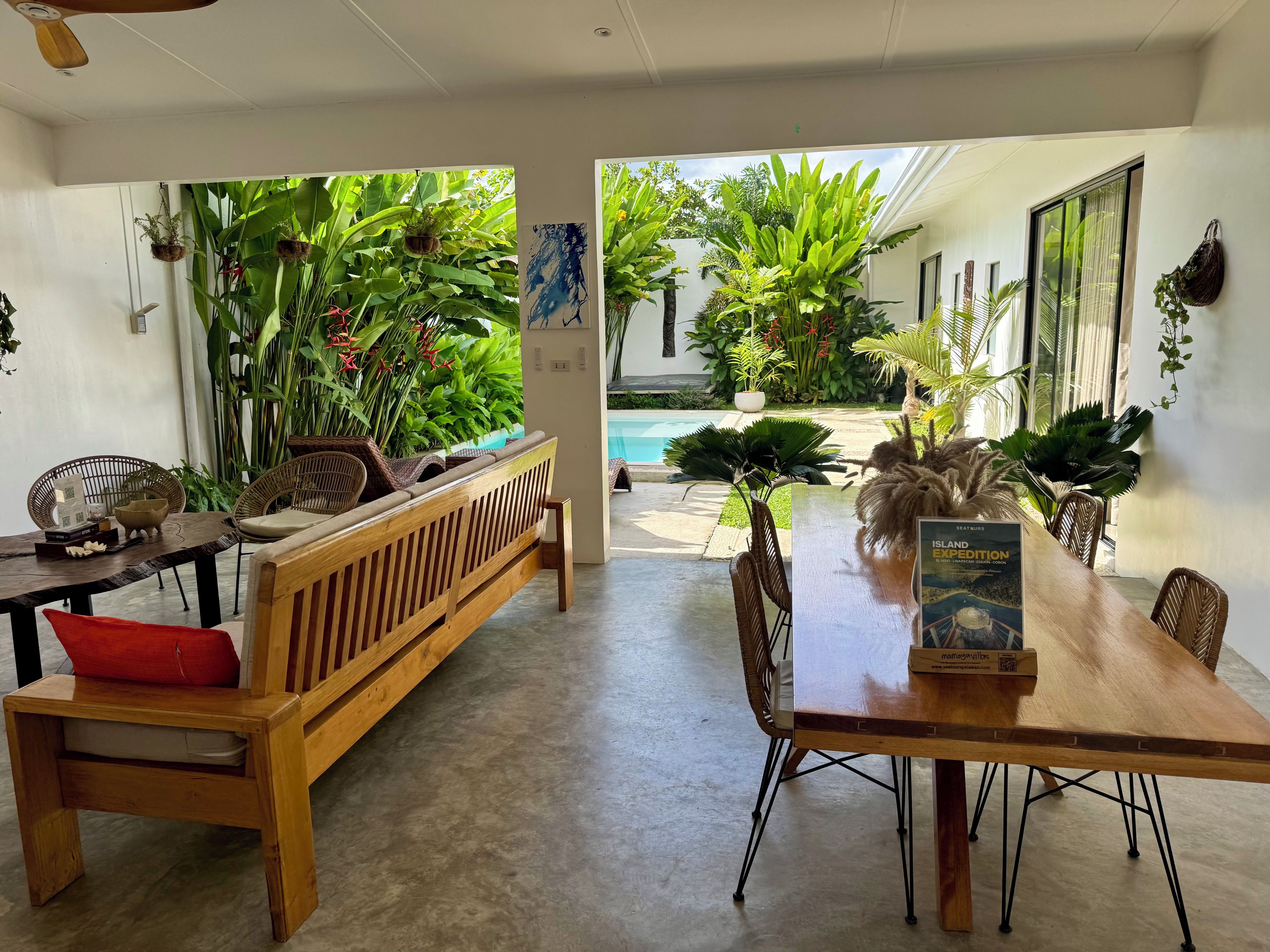 Un comedor con una mesa y sillas de madera, un banco y plantas en macetas.