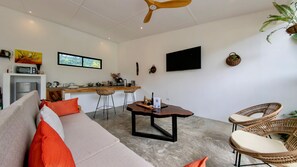 Un espacio de estar moderno con sofá, mesa de comedor, sillas, una zona de cocina y un televisor de pantalla plana.